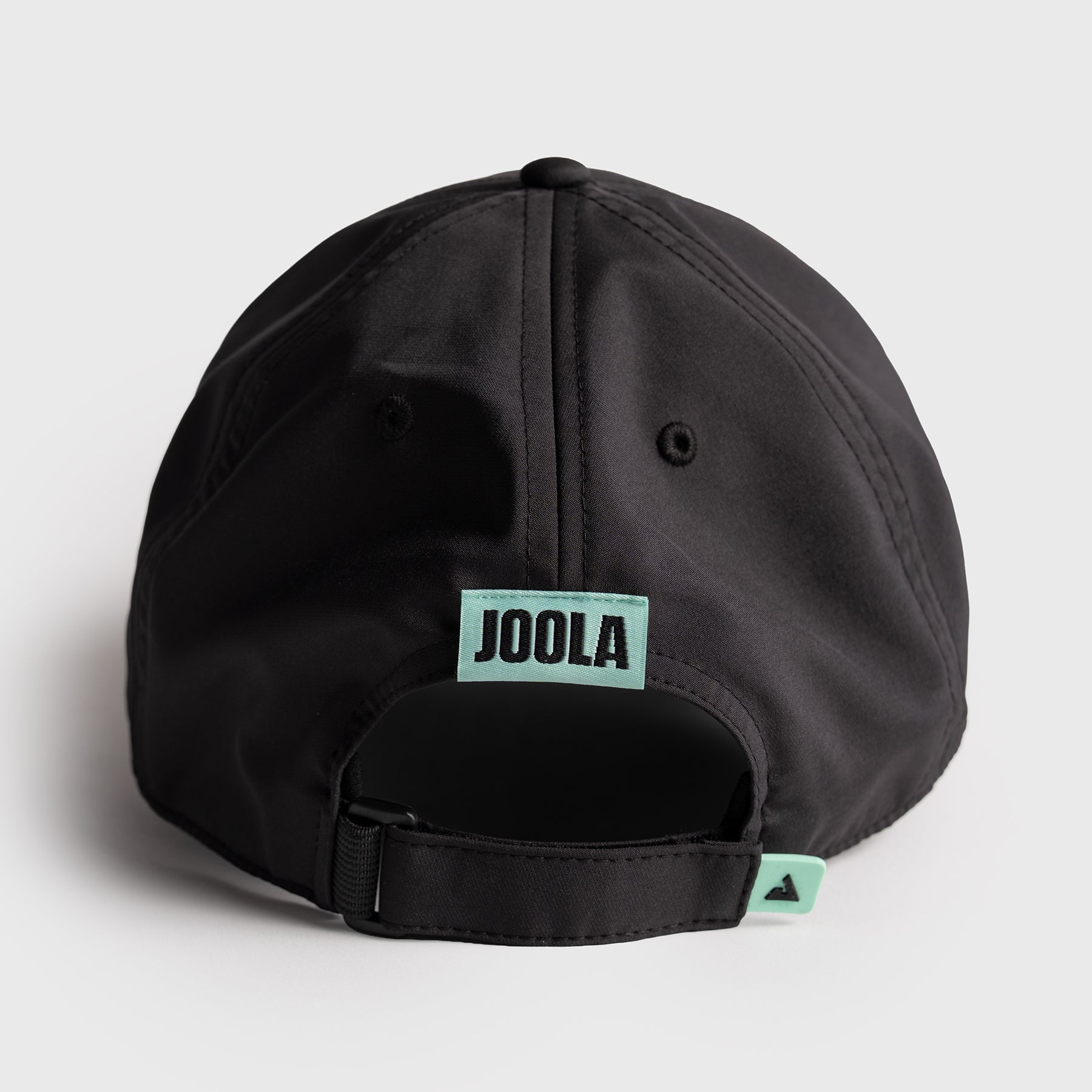Black cap with JOOLA logo on a light gray background, logo and tag are tourquiouse. 
