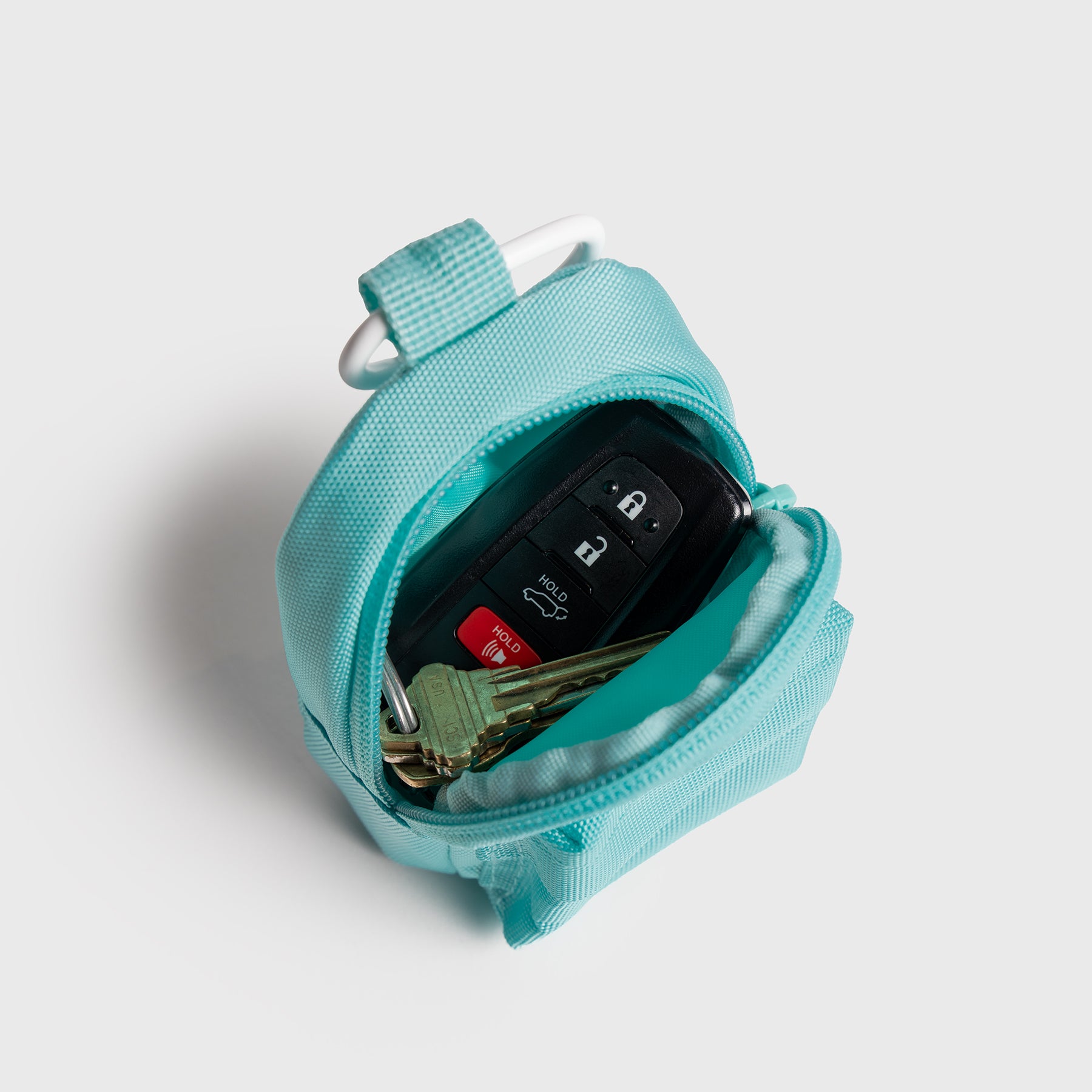 Turquoise JOOLA Micro bag, open with keys inside, with carabiner on a light gray background.