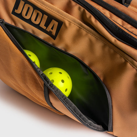 Zipper comparment holding two JOOLA pickleballs on the side of a JOOLA Latte colored pro pickleball tour bag.