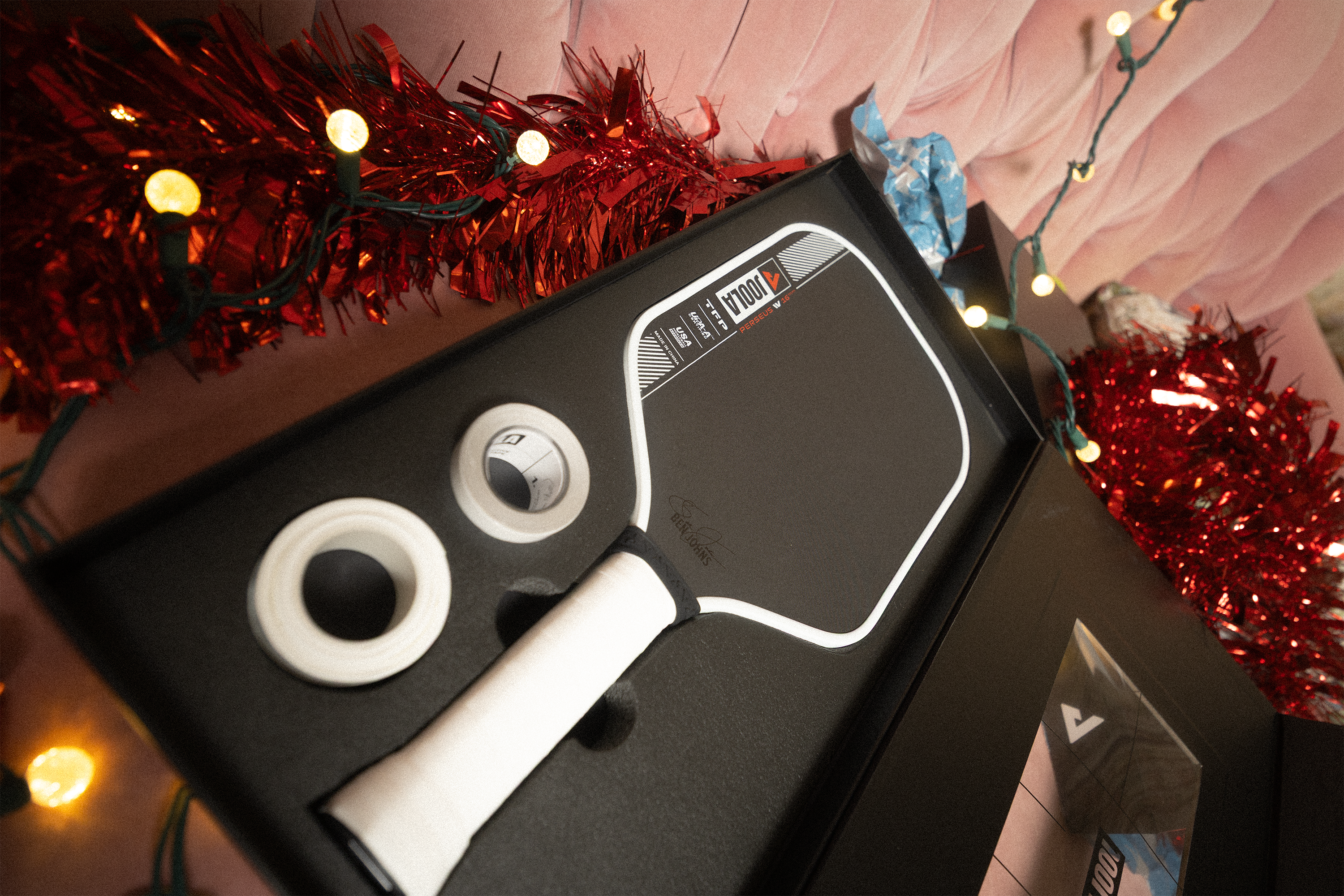 Holiday motif in the background, image of a JOOLA Perseus Pro IV pickleball paddle in its premium case with edge guard tape and overgrip.