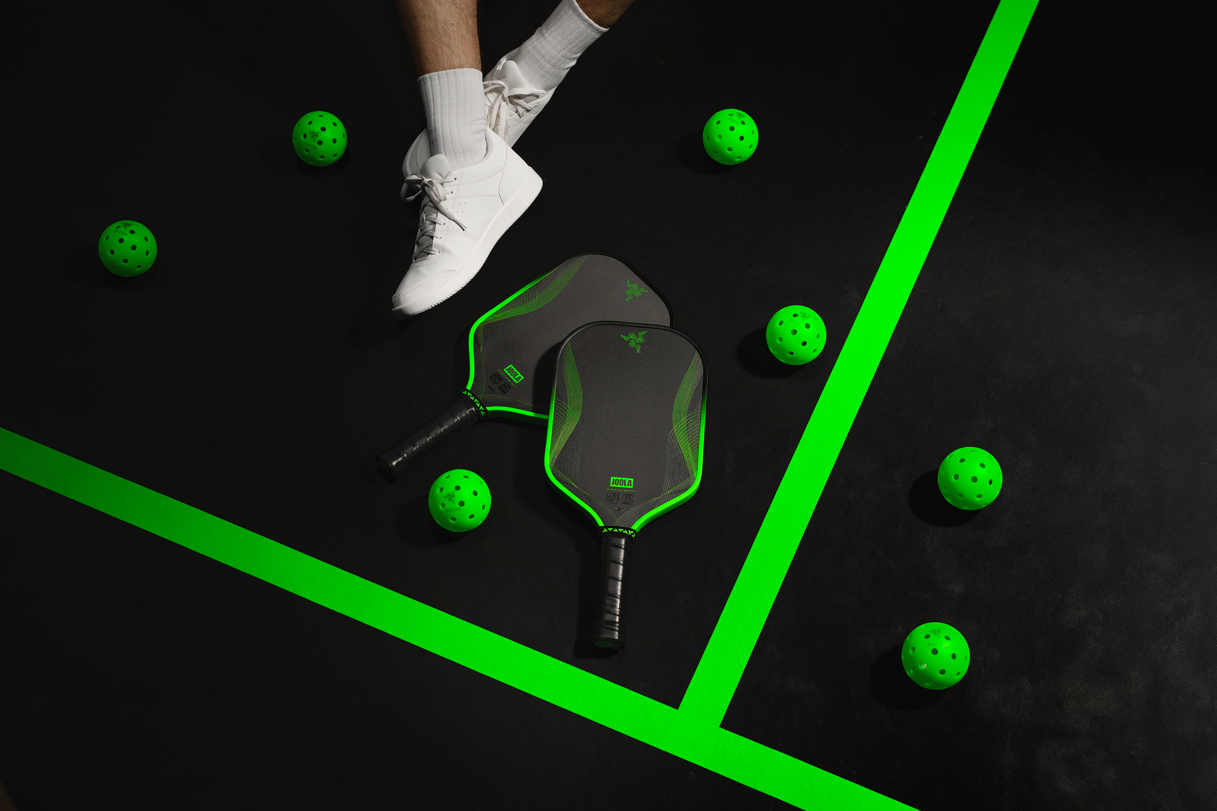 Pickleball paddle and balls on a black surface with green lines and highlights.