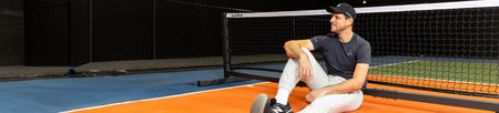 Horizontal banner image showing Dekel Bar leaning against a JOOLA Pickleball net.