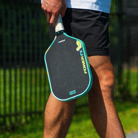 Close up on the JOOLA Power FX pickleball paddle by the legs of a male pickleball player.