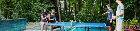 A group of four people playing table tennis outside on a JOOLA table tennis table.