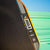 Close up image of the JOOLA Perseus Summer Daze Pickleball paddle with black surface, orange, blue, green and yellow color gradient on the rim, and white handle with a green and blue unfocused image in the background.