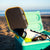 JOOLA Perseus Summer Daze Pickleball paddle with black surface, orange, blue, green and yellow color gradient on the rim, and white handle in an open cooler with items including sunglasses, and a bottle on a beach. 