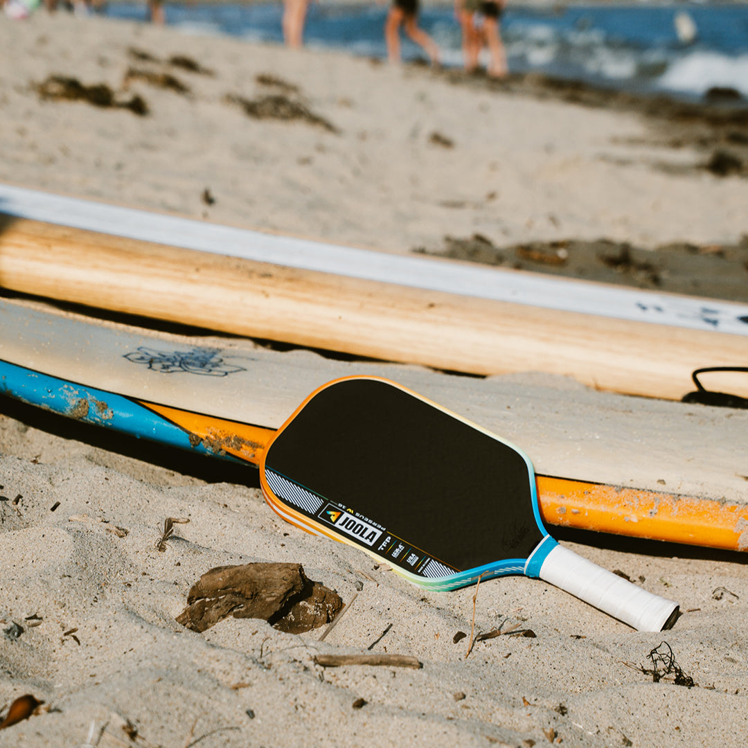 The JOOLA Perseus Summer Daze Pickleball paddle with black surface, orange, blue, green and yellow color gradient on the rim, and white handle.