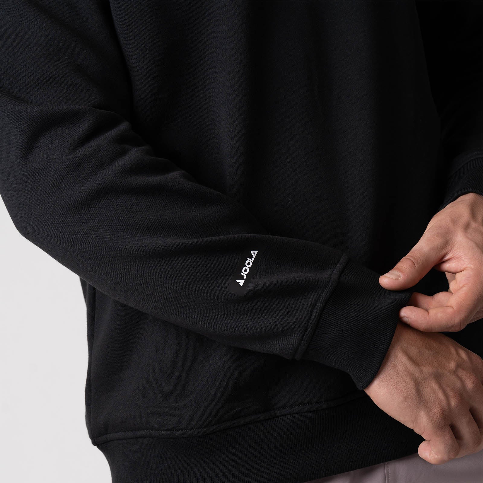 Close up image of the JOOLA logo on the right sleeve of the JOOLA Unisex Fleece Crew, Black.