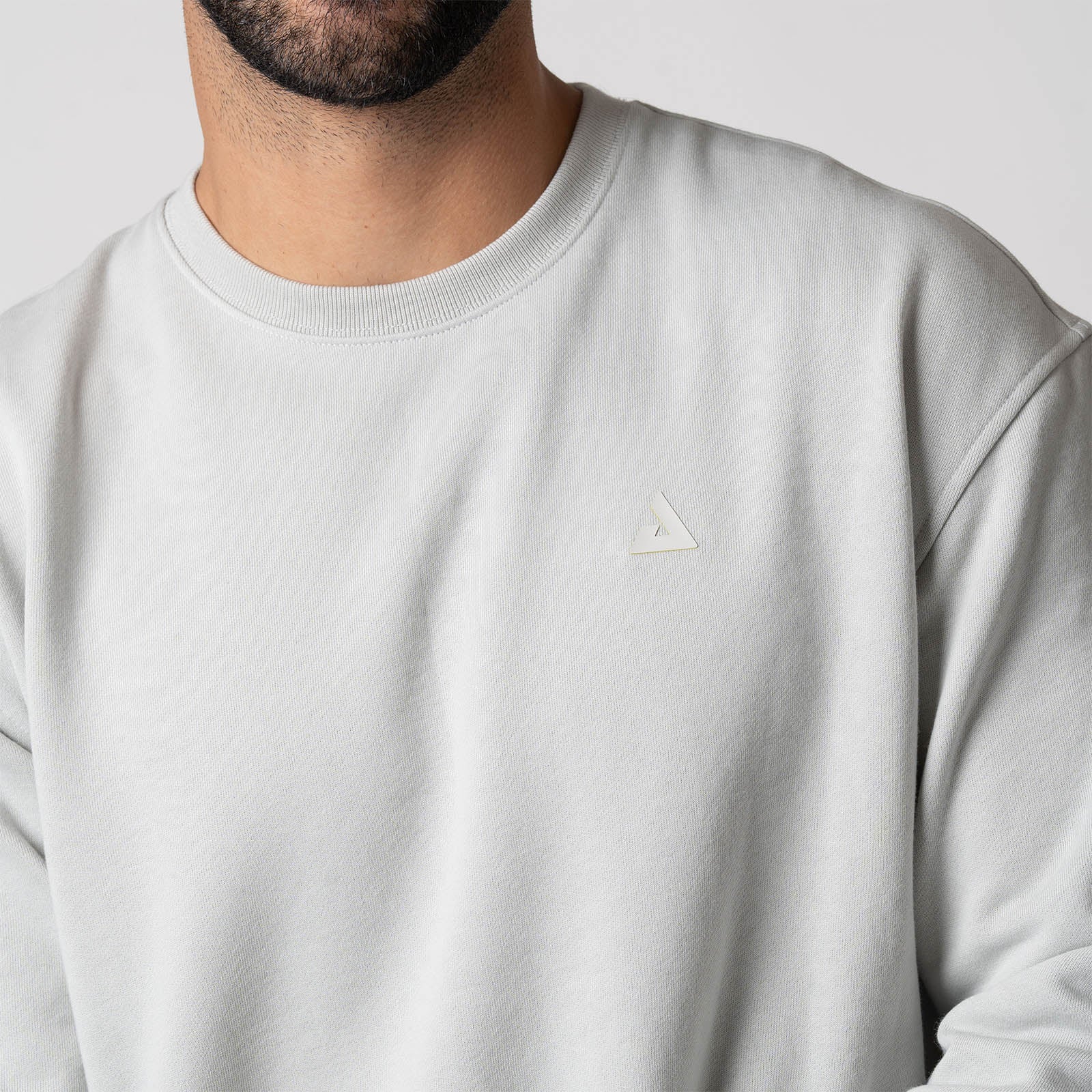 Close up image of the raised JOOLA Trinity logo on the left chest of a JOOLA Unisex Fleece Crew, Gravity Grey.