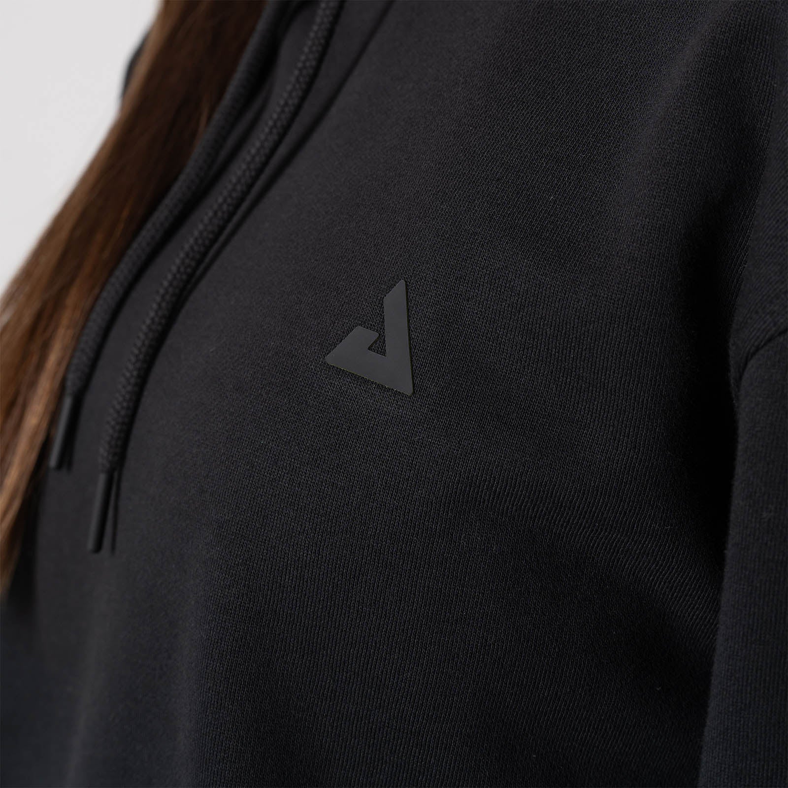 Close up on the raised JOOLA Trinity logo on the front of the JOOLA Unisex Fleece Hoodie, Black.