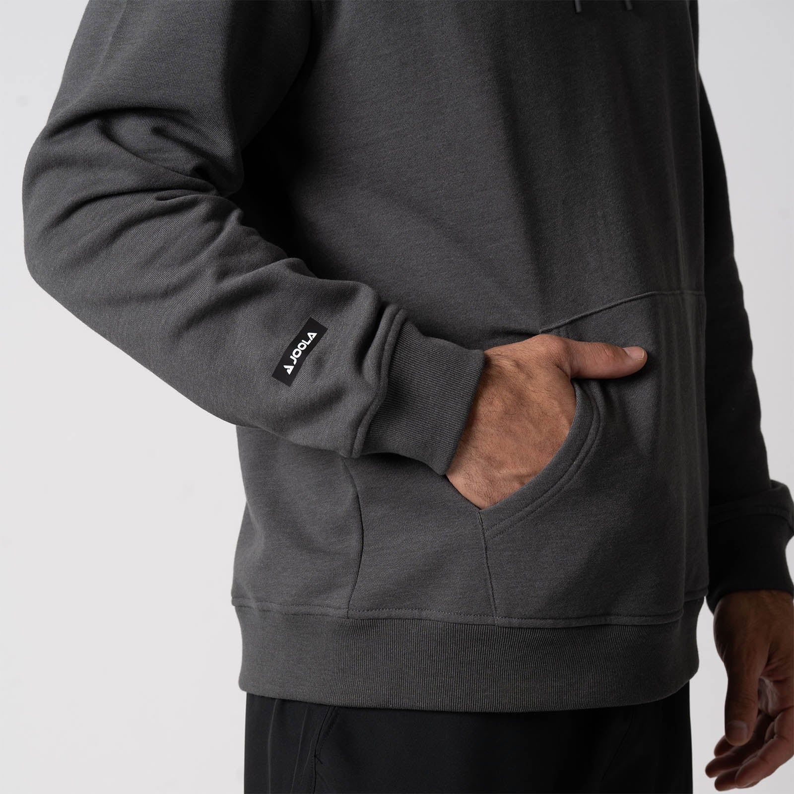 Close up image of male models hand inside the kangaroo pocket of the JOOLA Unisex Fleece Hoodie, Charcoal Heather.