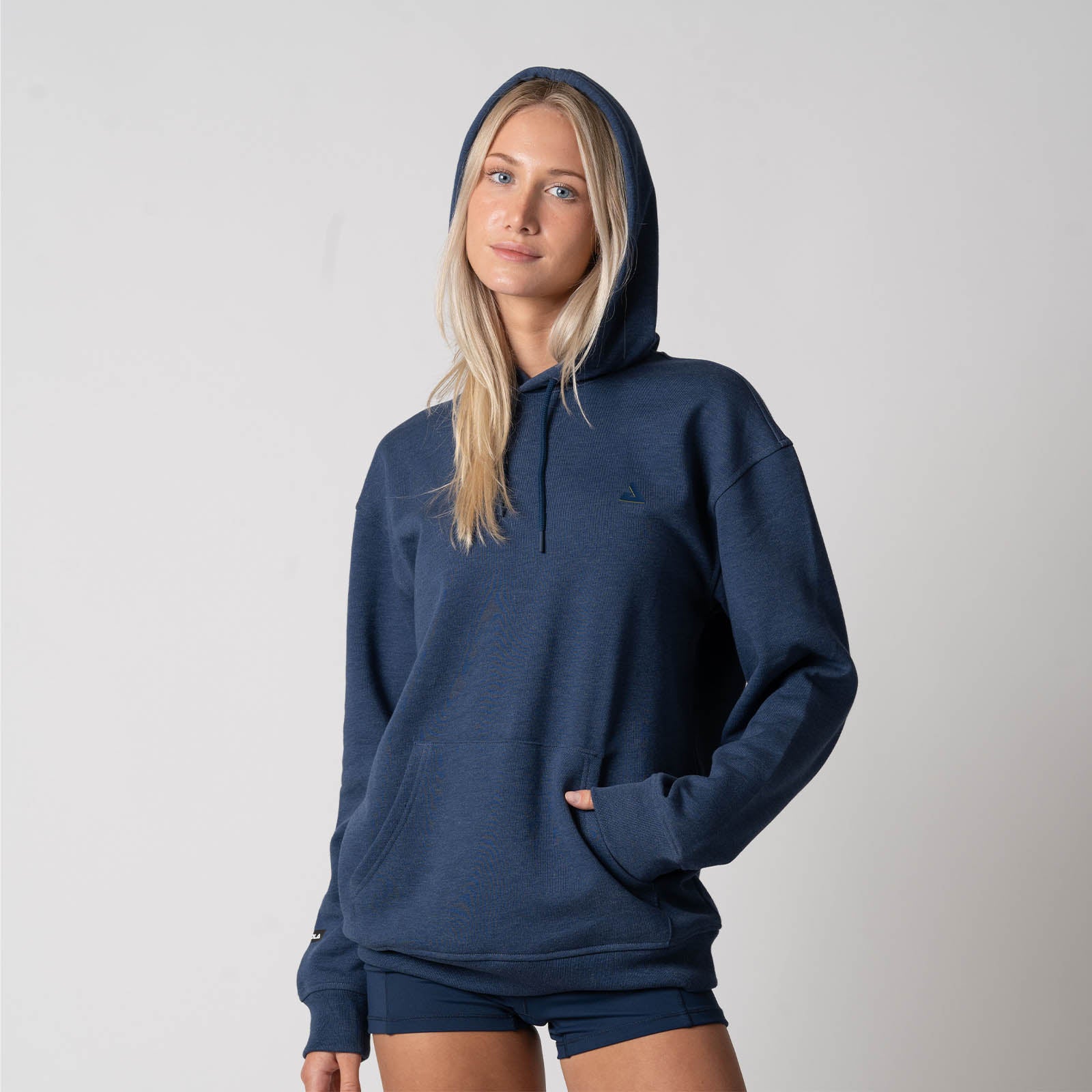 Image showing a female model wearing the JOOLA Unisex Fleece Hoodie, model has one hand inside the kangaroo pocket and the hood up, Navy.