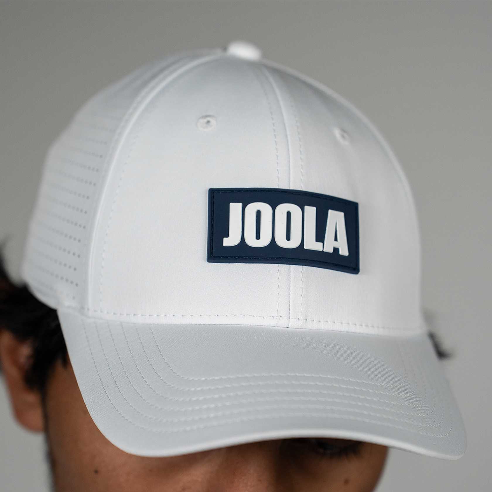 White cap with JOOLA logo on a gray background.