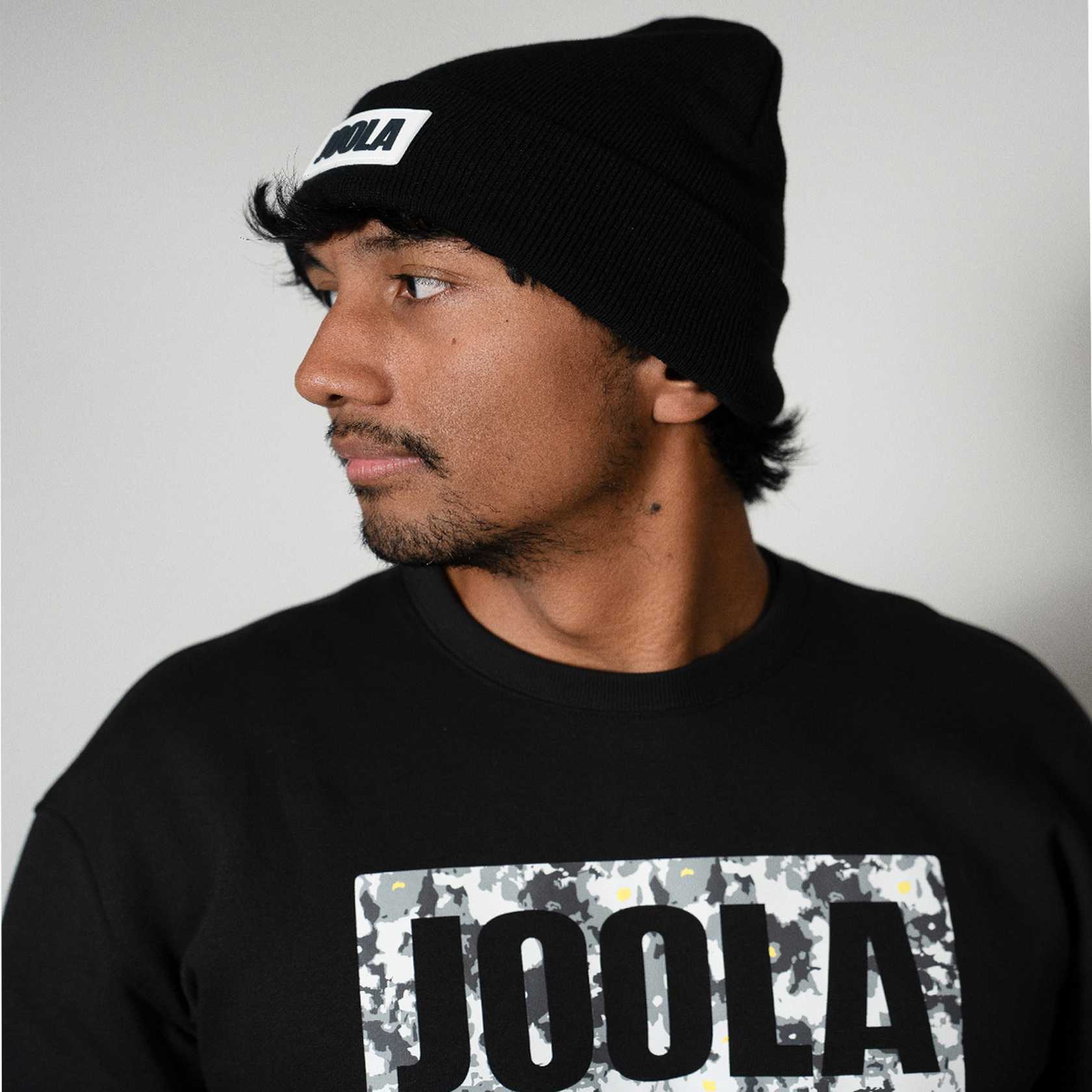 Gray background, man wearing a black JOOLA fleece sweatshirt and JOOLA beanie, black.