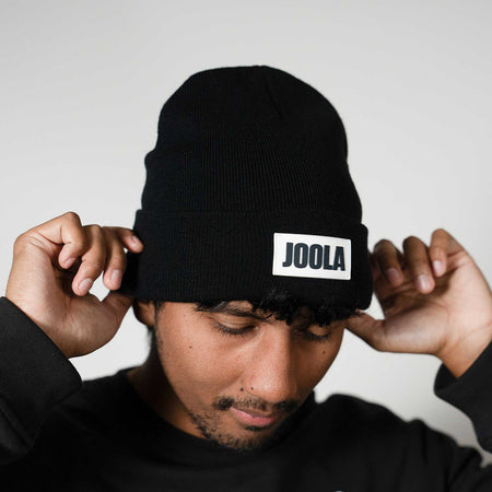 Gray background, image of a man wearing a Black JOOLA branded beanie.