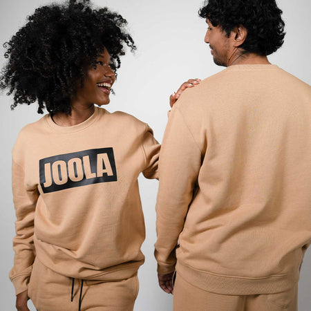 Two people wearing matching latte colored sweatsuits with 'JOOLA' branding on a plain background
