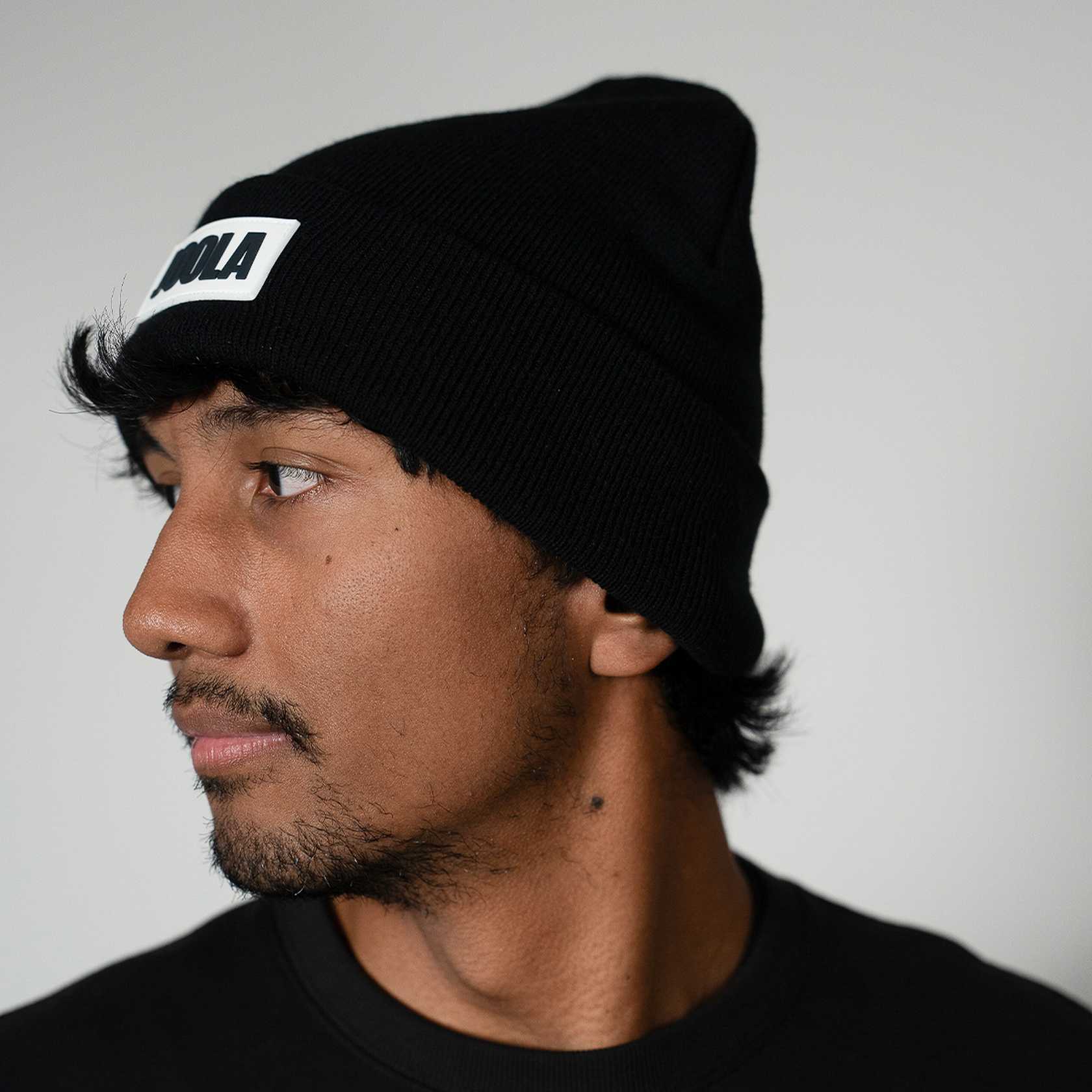 Person wearing a black beanie with a JOOLA logo on a plain background
