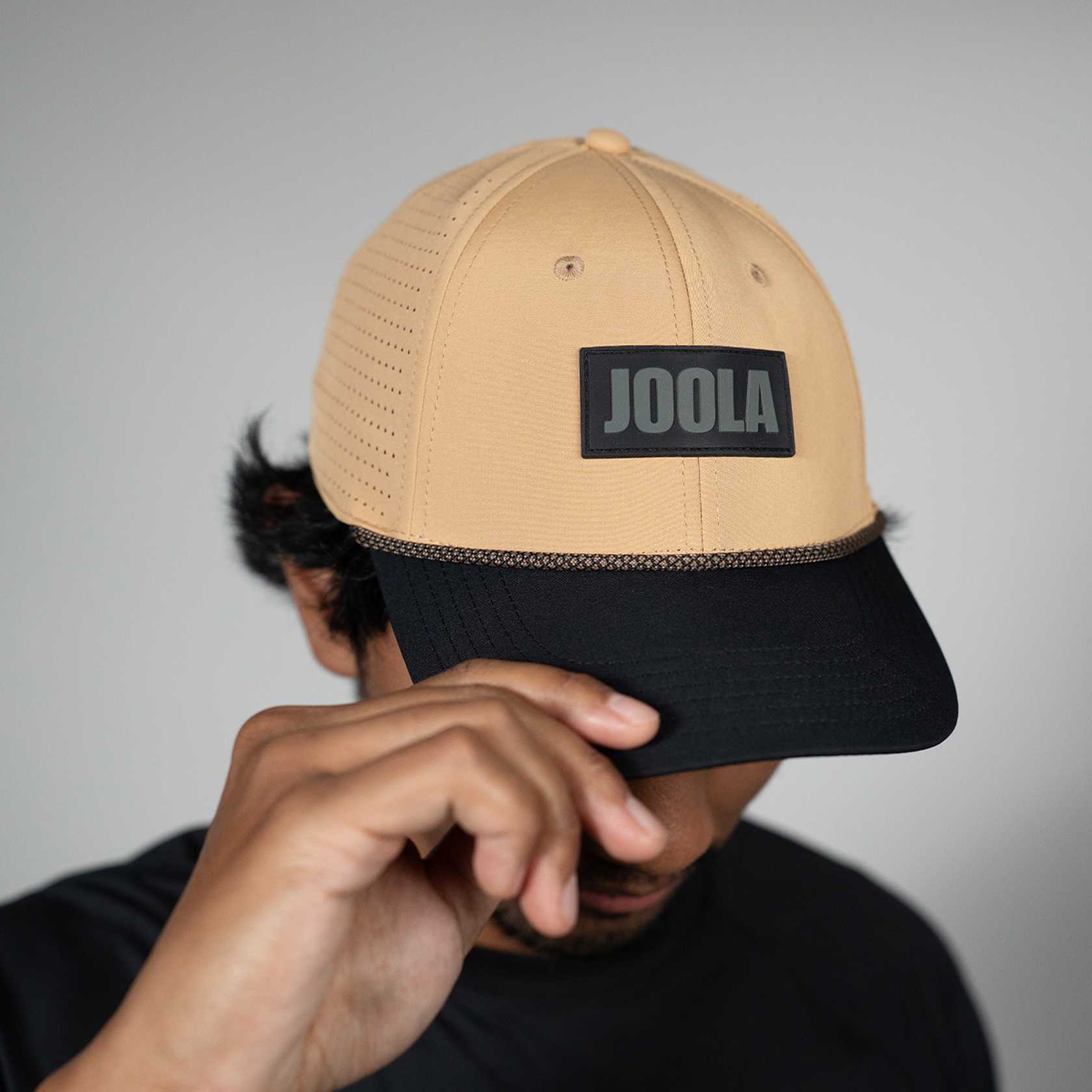 Latte and black cap with 'JOOLA' logo held by a person against a gray background