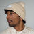 Person wearing a latte colored beanie with a brand logo on a gray background