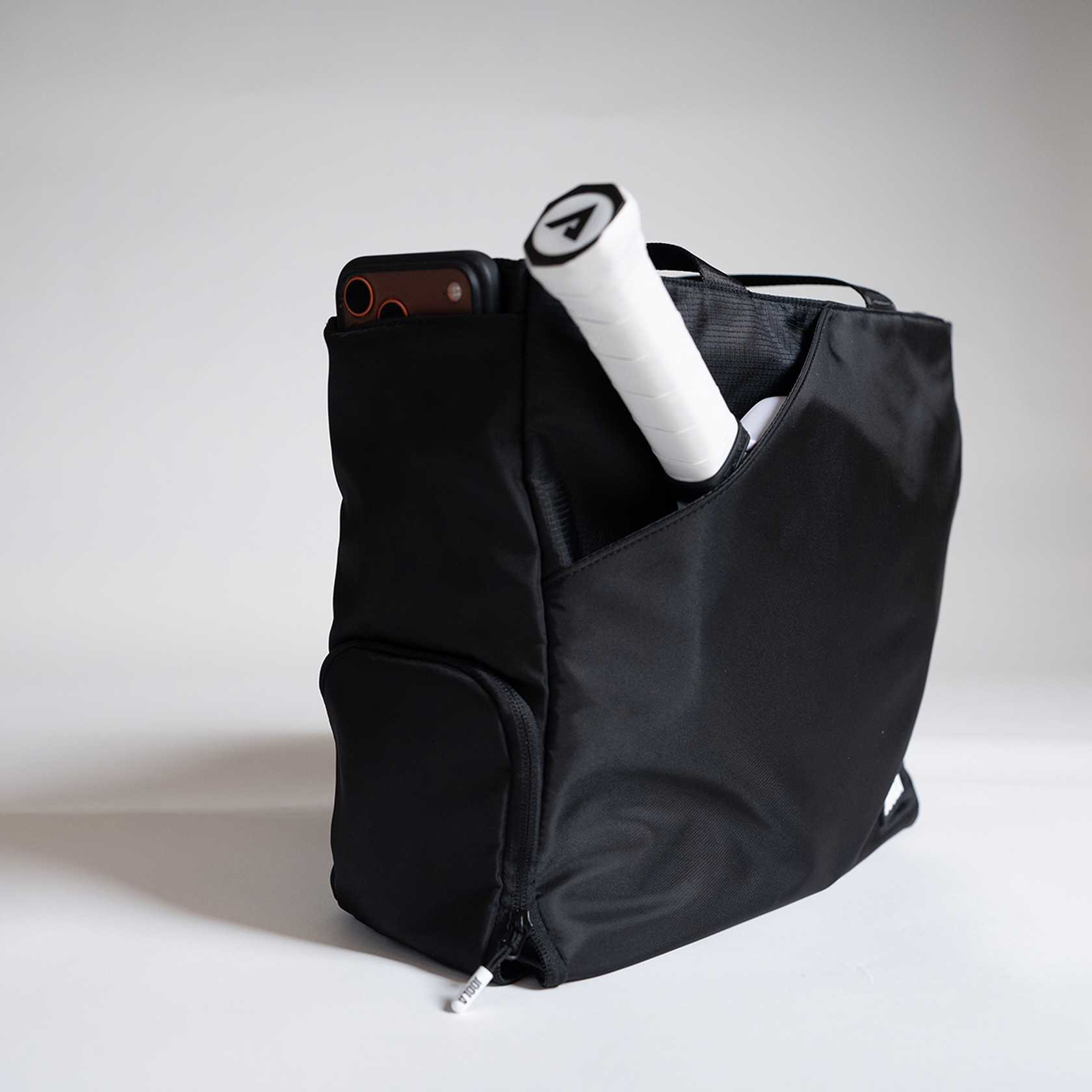 Black backpack with a phone and pickleball paddle on a light gray background