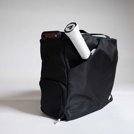 Black backpack with a phone and pickleball paddle on a light gray background