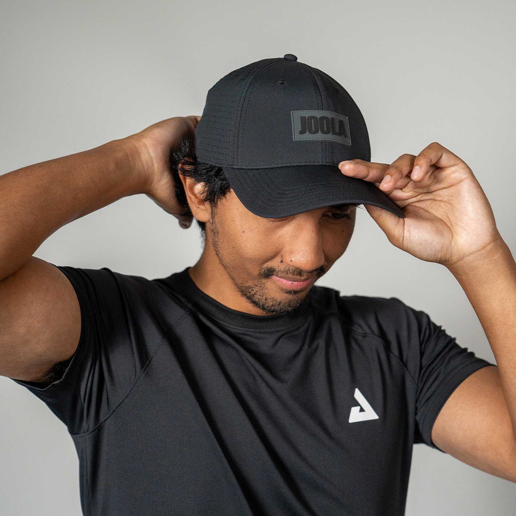 Man wearing a black cap with 'JOOLA' logo and black t-shirt with white logo on gray background