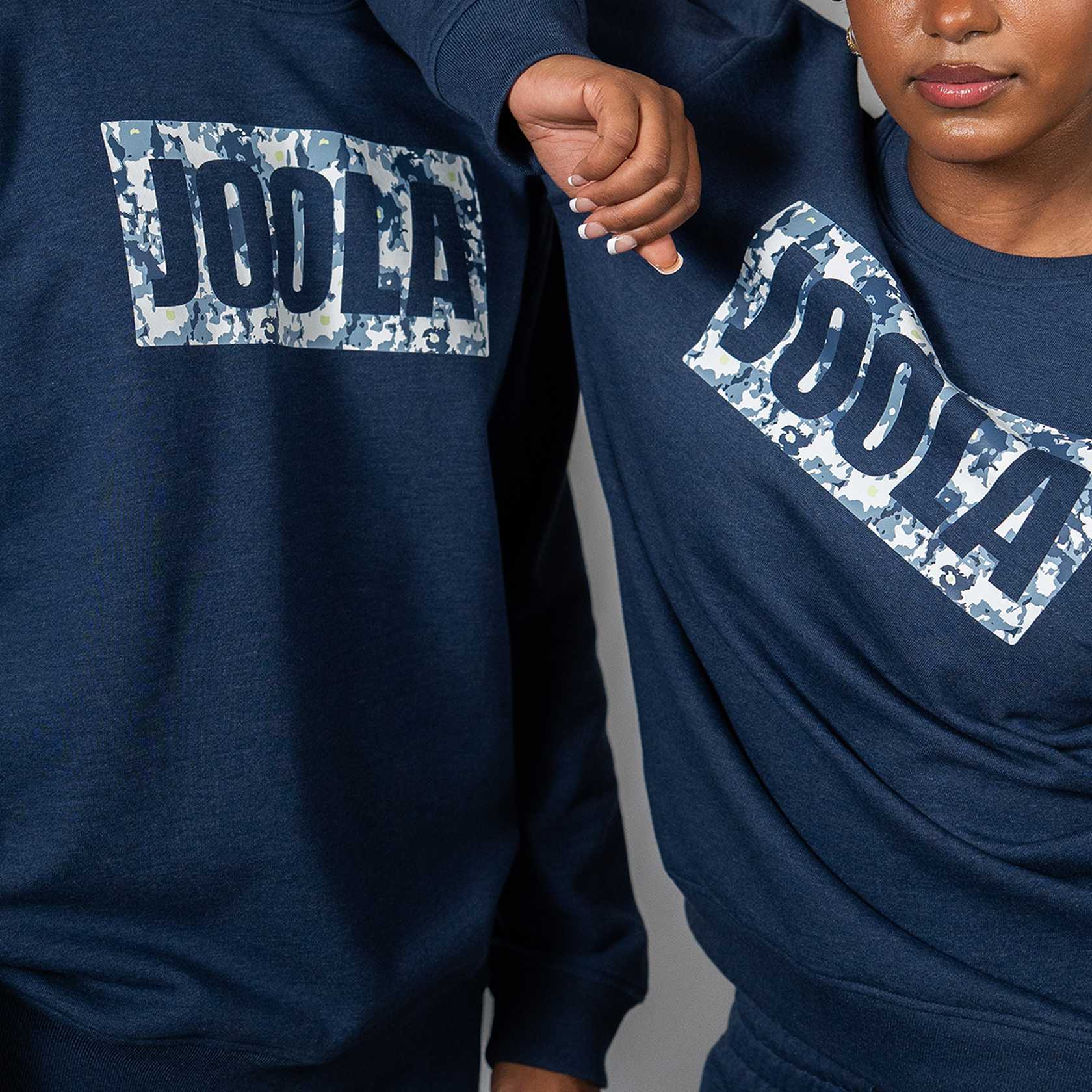 Two people wearing fleece navy blue sweatshirts with JOOLA printed on them against a gray background.