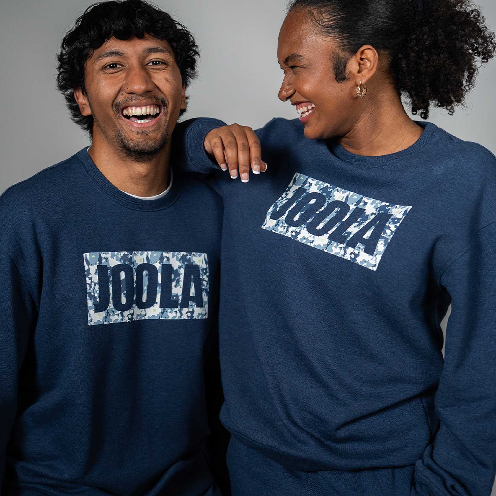 Two people wearing navy blue fleece sweatshirts with JOOLA logo on a gray background