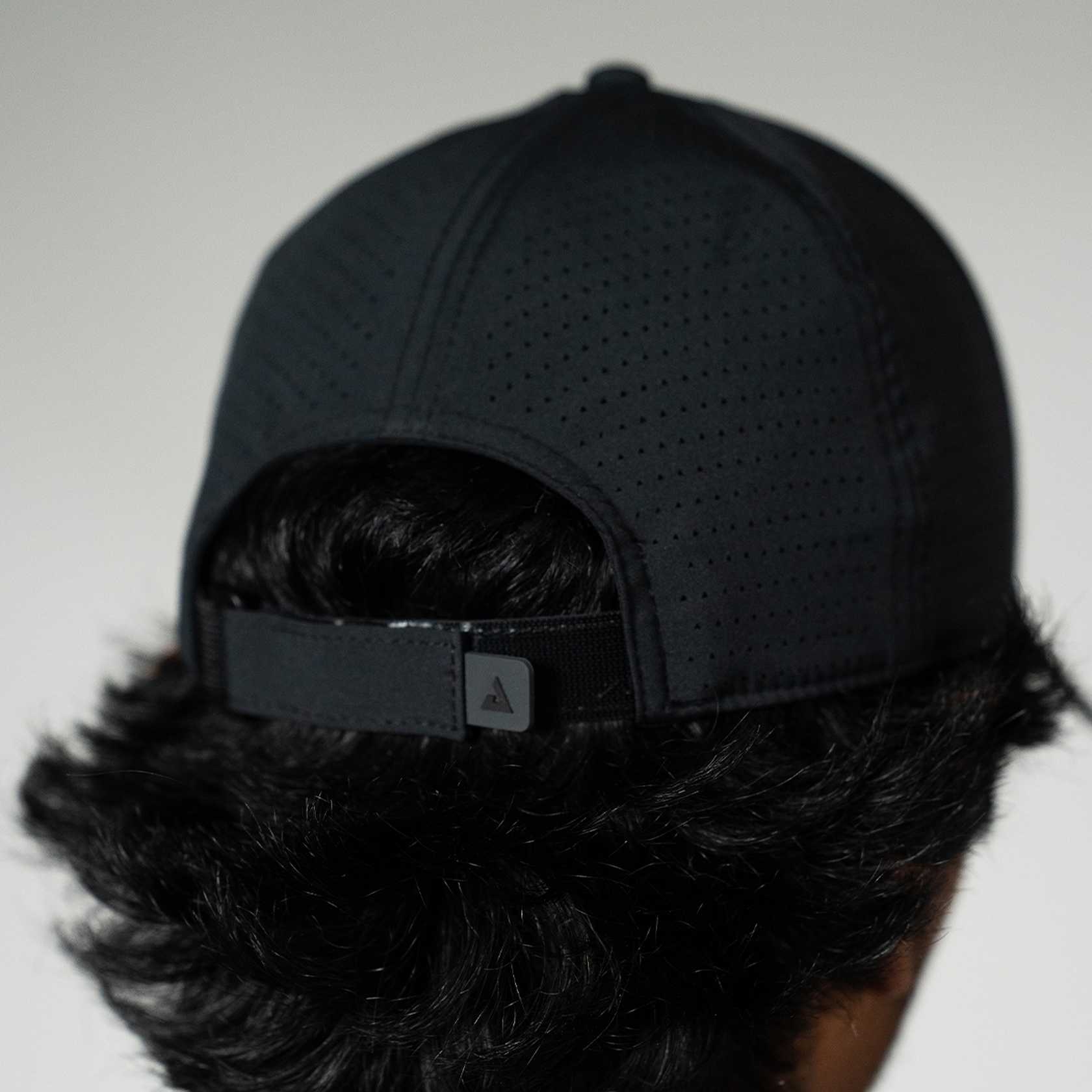 Person wearing a black cap with a brand logo on a plain background