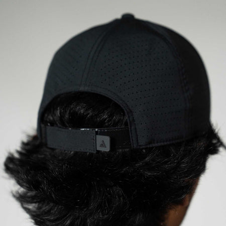 Person wearing a black cap with a brand logo on a plain background