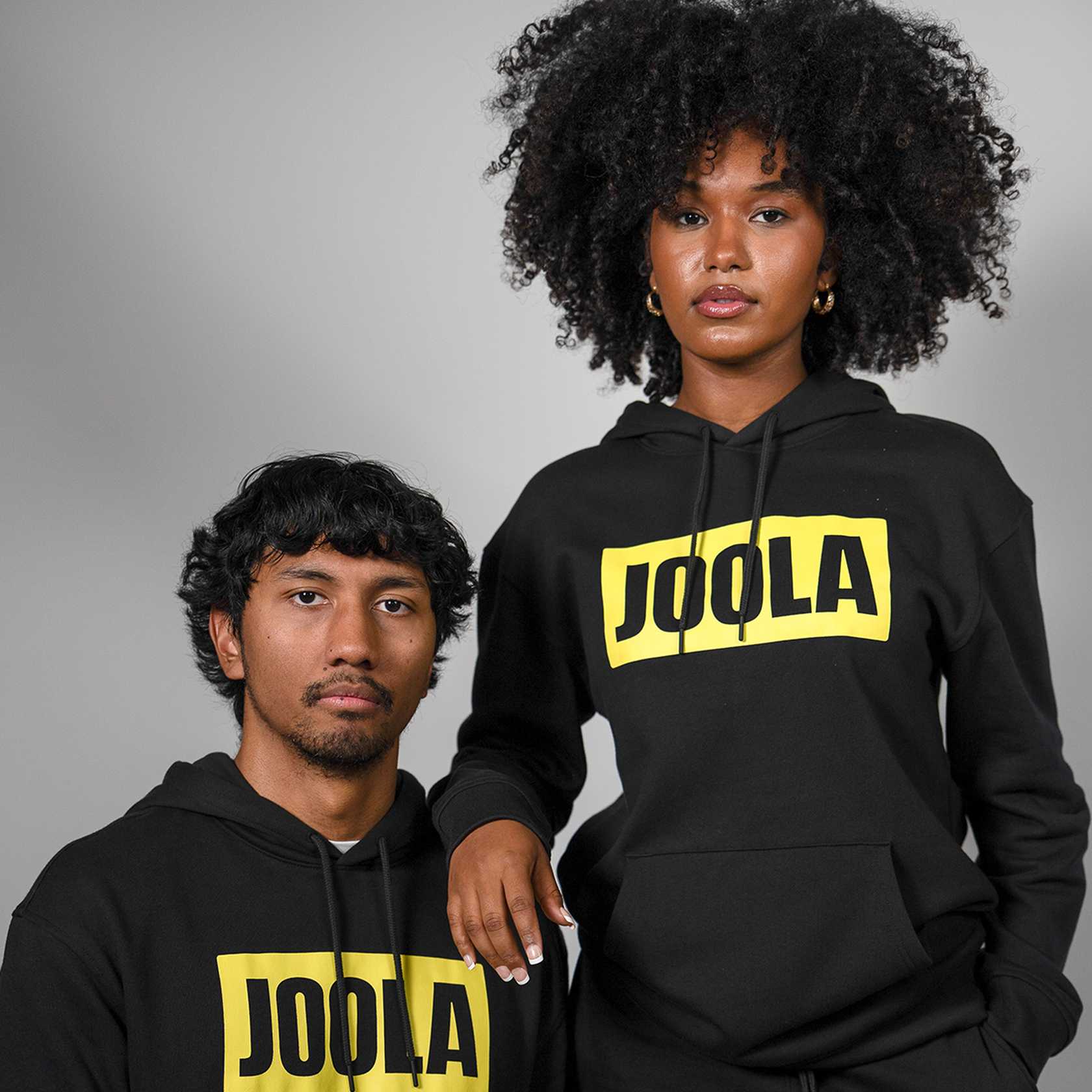 Two people wearing black hoodies with 'JOOLA' logo on a gray background