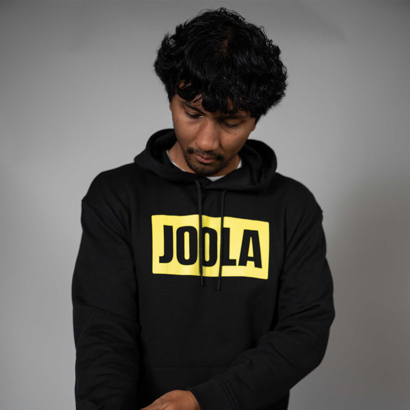 Person wearing a black hoodie with 'JODLA' in yellow on a gray background