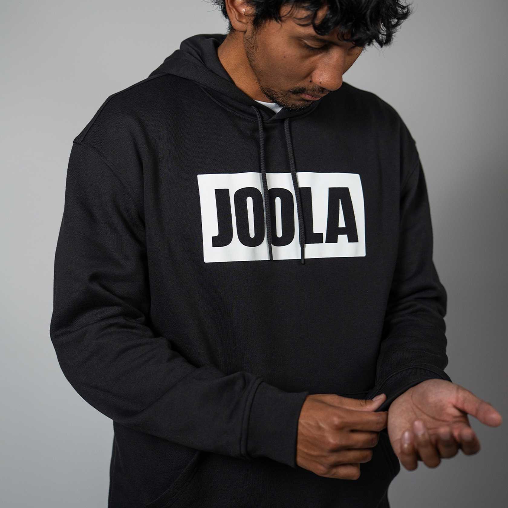 Person wearing a black hoodie with 'JOOLA' logo on a gray background