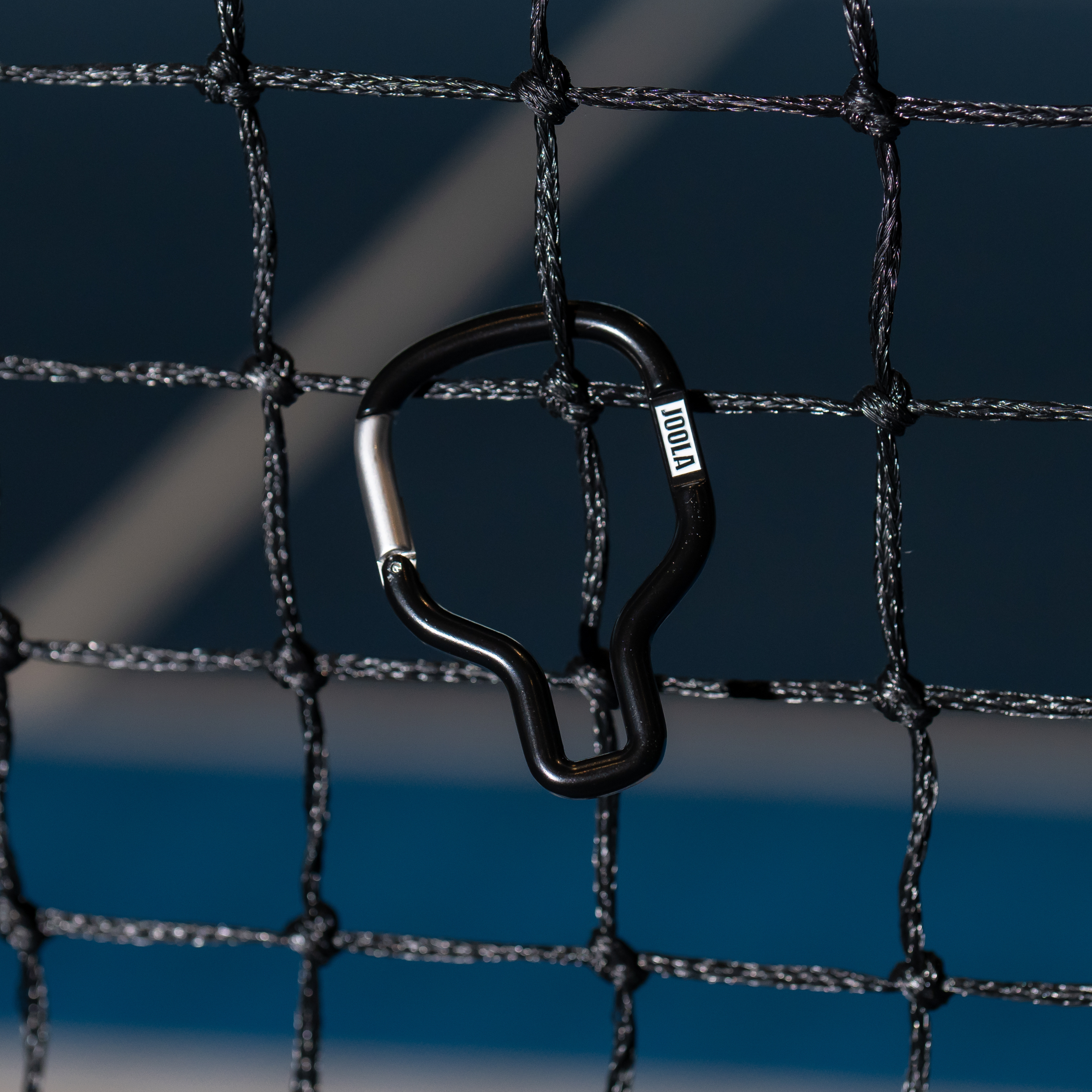 Black and white JOOLA pickleball paddle caribinar handing off a pickleball net.