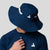Man wearing a navy blue JOOLA wide brim hat with black accents on a light gray background