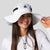 Woman wearing a JOOLA wide brim hat with black accents on a light gray background