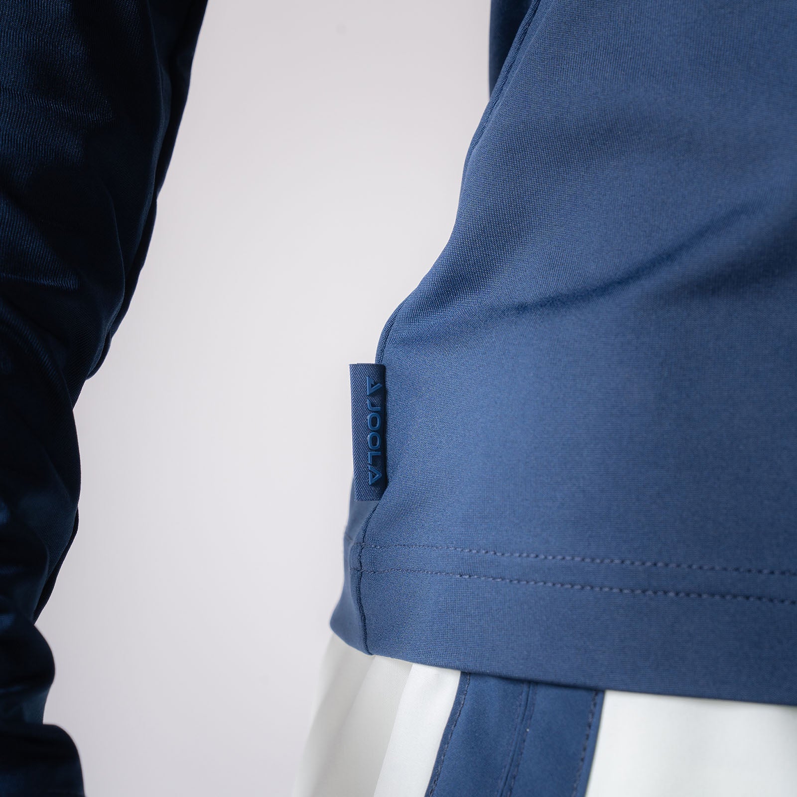 Close up image showing the raised JOOLA logo tag on the side of a JOOLA Women's Quarter Zip Pullover, Navy.