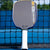 Image of a JOOLA Dual Signature Kate Fahey and Brooke Buckner Agassi Pro V pickleball paddle resting against a pickleball net.