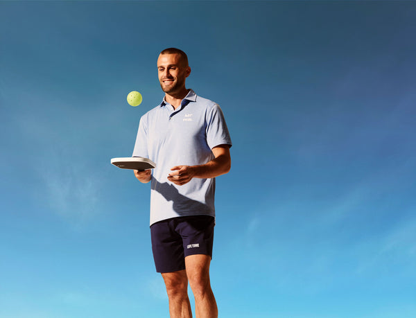 Male pickleball player bouncing the pickleball off a paddle with the blue sky in the background.