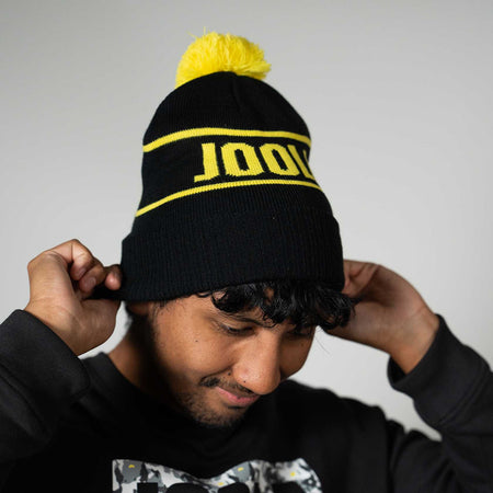 Person wearing a black beanie with yellow pom-pom and JOOLA text, against a plain background
