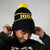 Person wearing a black beanie with yellow pom-pom and JOOLA text, against a plain background