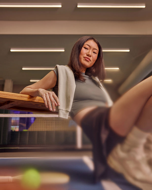 Female pickleball player leaning on a bench at an indoor pickleball court.