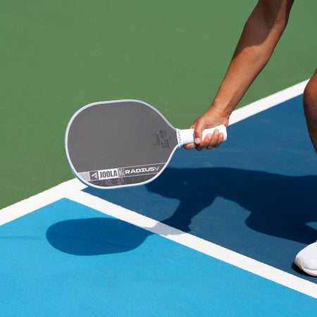 A close-up action shot of a pickleball player holding a gray and white Radswell paddle on a blue and green pickleball court.