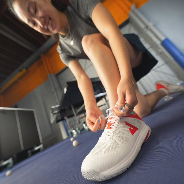 Image of JOOLA Table Tennis pro tying her white and red JOOLA TT SM4SH table tennis shoe.